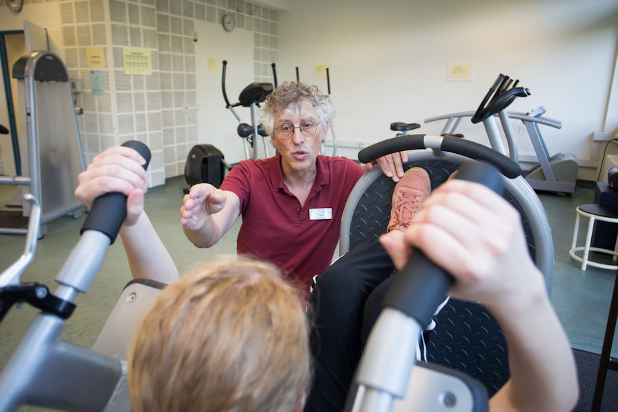 Eine Rehabilitandin beim Trainieren im Fitnessstudio mit dem Therapeuten an der Seite Eine Rehabilitandin beim Trainieren im Fitnessstudio mit dem Therapeuten an der Seite